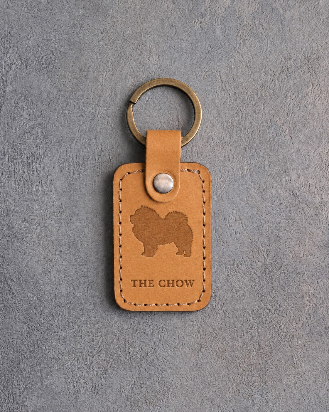 Indian Summer tan leather keychain debossed with a Chow Chow silhouette above THE CHOW, on gray concrete