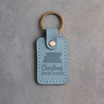 Turquoise leather keychain debossed with a stack of books above Christmas and BOOK FLOOD, on gray concrete