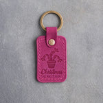 Fuchsia leather keychain debossed with a potted Christmas cactus in bloom above Christmas CACTUS, on gray concrete