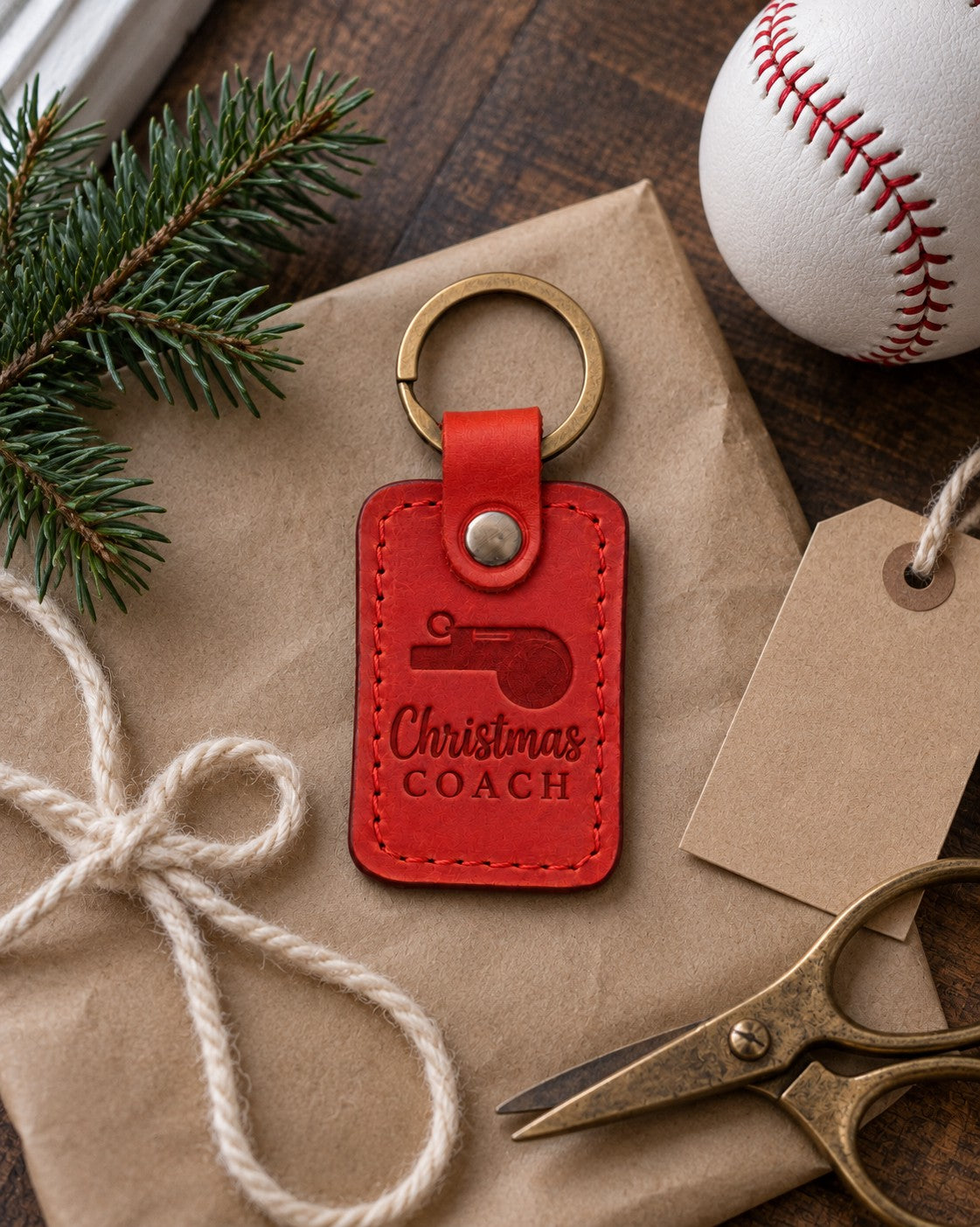Red Christmas Coach keychain on brown kraft paper beside a fir sprig and a blank kraft gift tag