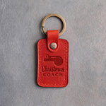 Poppy red leather keychain debossed with a coach's whistle and the words Christmas COACH, on gray plaster