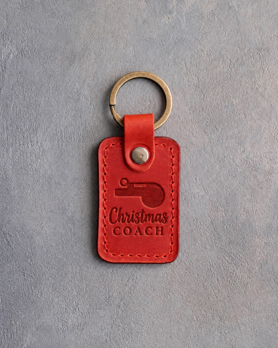 Poppy red leather keychain debossed with a coach's whistle and the words Christmas COACH, on gray plaster