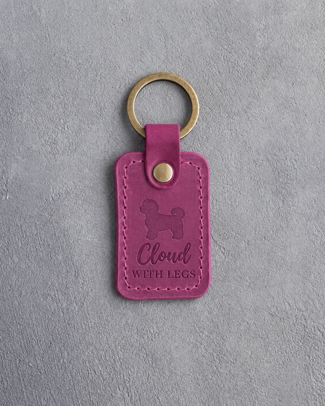 Fuchsia pink leather keychain debossed with a maltipoo and the words Cloud WITH LEGS, on gray concrete