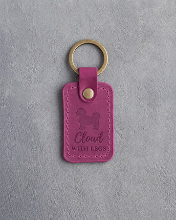 Fuchsia pink leather keychain debossed with a maltipoo and the words Cloud WITH LEGS, on gray concrete