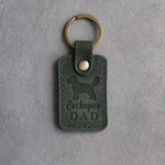 Forest green leather keychain debossed with a cockapoo silhouette and Cockapoo DAD on gray concrete