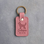 Parisian Blossom pink leather keychain with a debossed cockapoo and the words Cockapoo MOM, on gray concrete