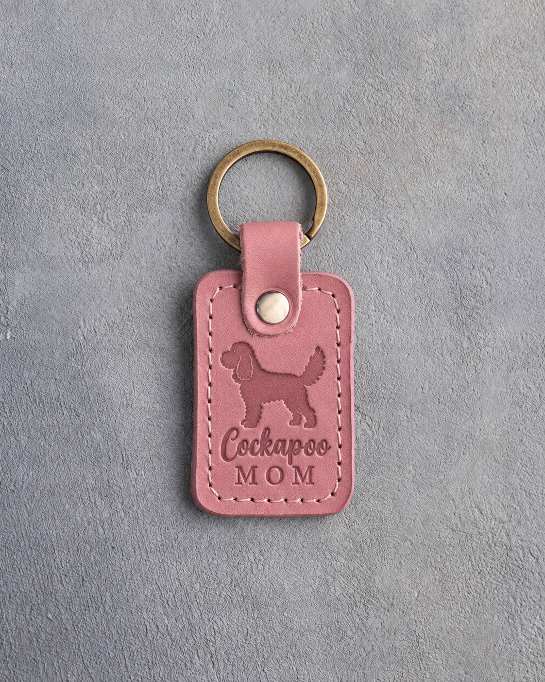 Parisian Blossom pink leather keychain with a debossed cockapoo and the words Cockapoo MOM, on gray concrete