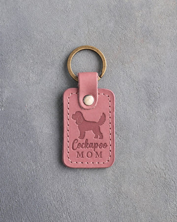 Parisian Blossom pink leather keychain with a debossed cockapoo and the words Cockapoo MOM, on gray concrete