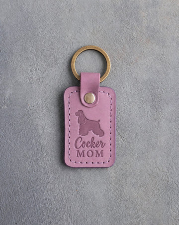 Lilac leather keychain with a debossed cocker spaniel and the words Cocker MOM, on gray concrete