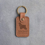 Caramel leather keychain debossed with a long-eared cocker spaniel over Cocker Spaniel and THE COCKER, on gray concrete
