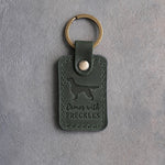 Forest green leather keychain debossed with an English Setter silhouette and the words Comes with FRECKLES, on gray concrete
