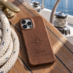 Sicilian brown Wes TRUE NORTH iPhone case in full-grain leather on the worn teak cockpit table of a sailboat beside a coiled white dock line
