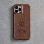 Back of a Sicilian brown leather iPhone case debossed with an eight-point compass rose above Wes and TRUE NORTH below the camera, on gray plaster
