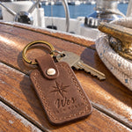 Sicilian brown Wes TRUE NORTH keychain in full-grain leather on the worn teak cockpit table of a sailboat beside a coiled white dock line