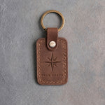 Sicilian brown leather keychain debossed with an eight-point compass rose above TRUE NORTH, on gray concrete
