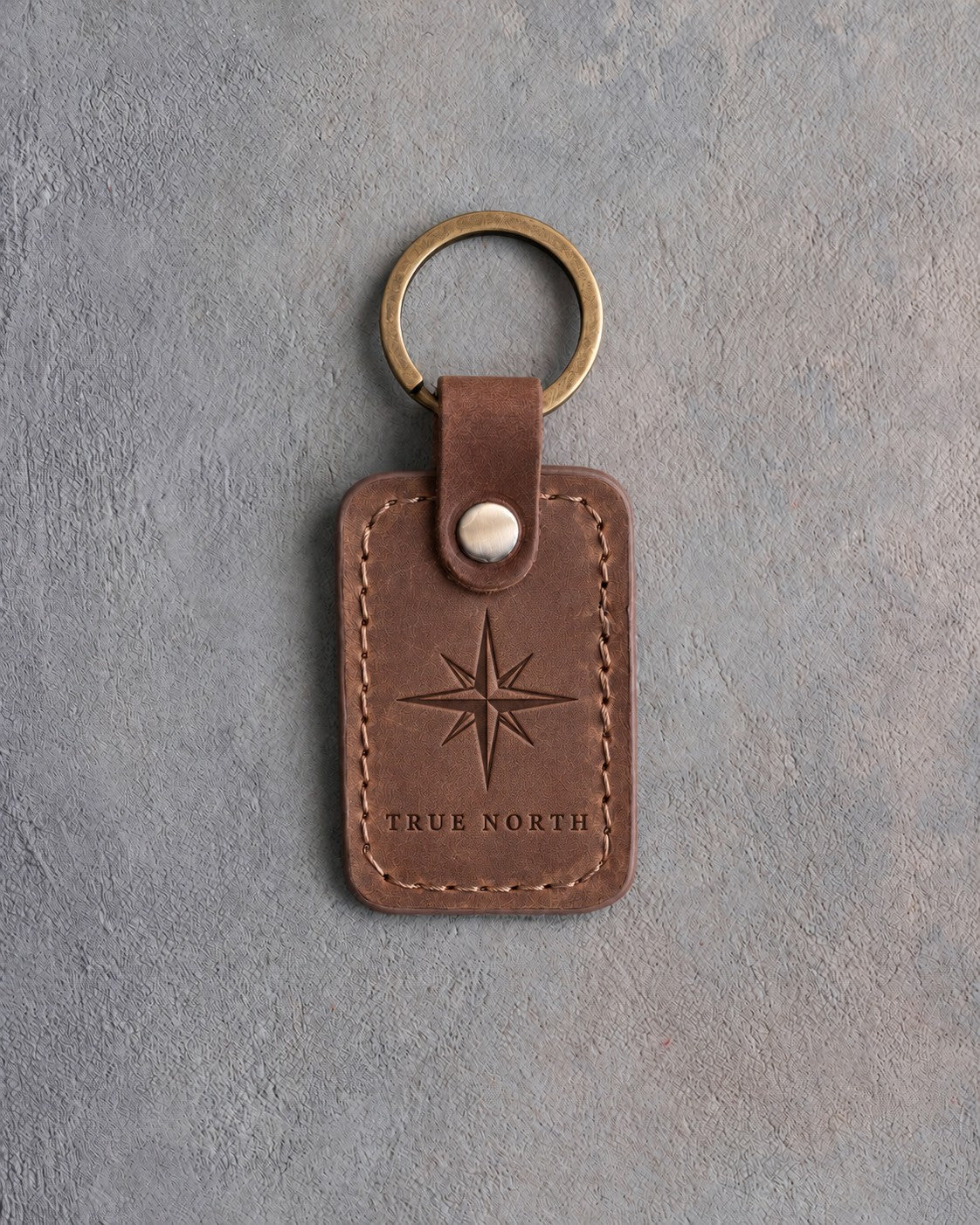 Sicilian brown leather keychain debossed with an eight-point compass rose above TRUE NORTH, on gray concrete