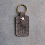 Country gray leather keychain debossed with a sitting dog in a cone collar and the words Cone of SHAME, on gray concrete