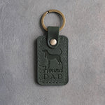 Forest green leather keychain debossed with a Coonhound silhouette and the words Hound DAD, on gray concrete