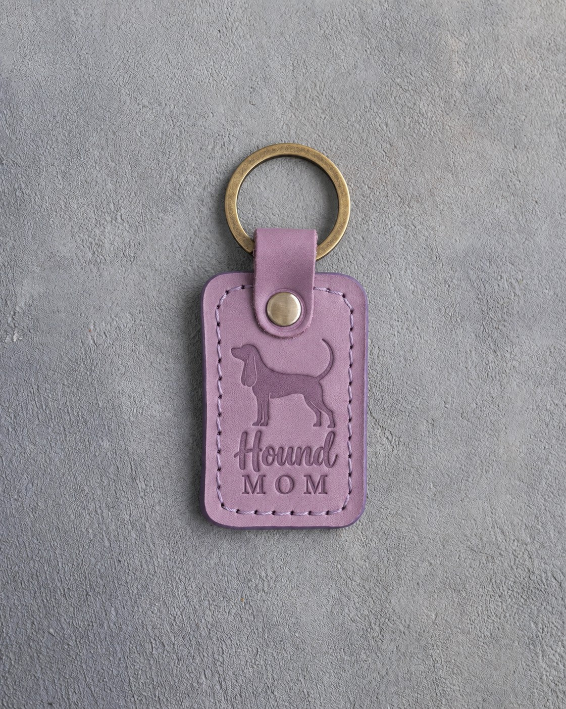 Lilac leather keychain debossed with a Coonhound silhouette and the words Hound MOM, on gray concrete