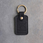 Black leather keychain debossed with a Coonhound silhouette above THE HOUND, on gray concrete