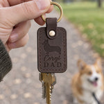 Dark brown Corgi Dad keychain held in a park with a corgi on a leash smiling in the background