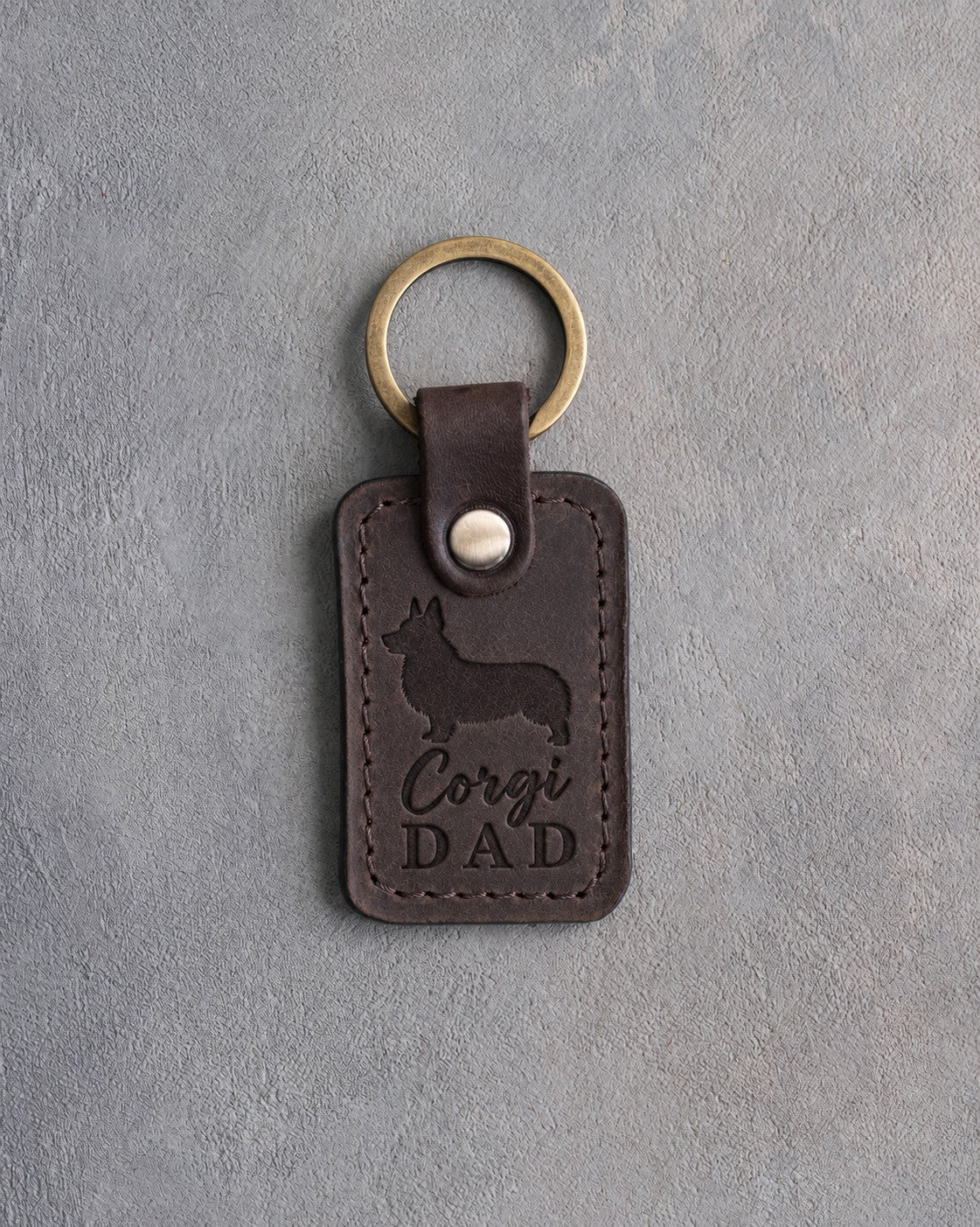 Dark espresso leather keychain debossed with a corgi silhouette and the words Corgi DAD, on gray concrete