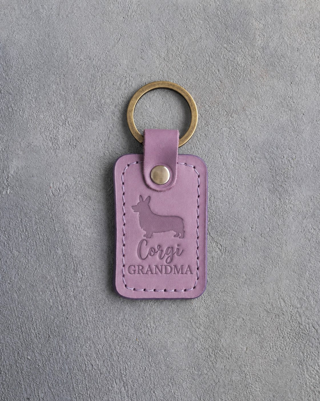 Lilac leather keychain debossed with a Pembroke corgi silhouette and the words Corgi GRANDMA, on gray concrete