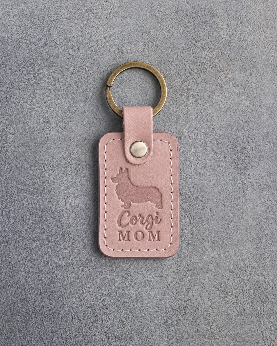 Blush pink leather keychain with a debossed Pembroke corgi silhouette and Corgi MOM lettering on gray concrete