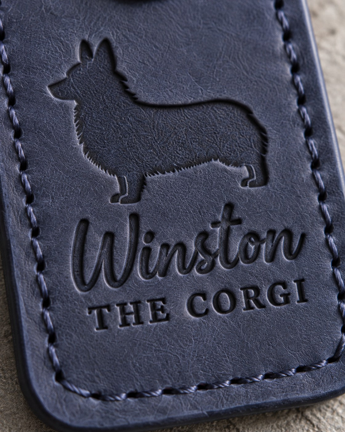 Close-up of Winston and THE CORGI debossed in navy full-grain leather below a tailless corgi silhouette