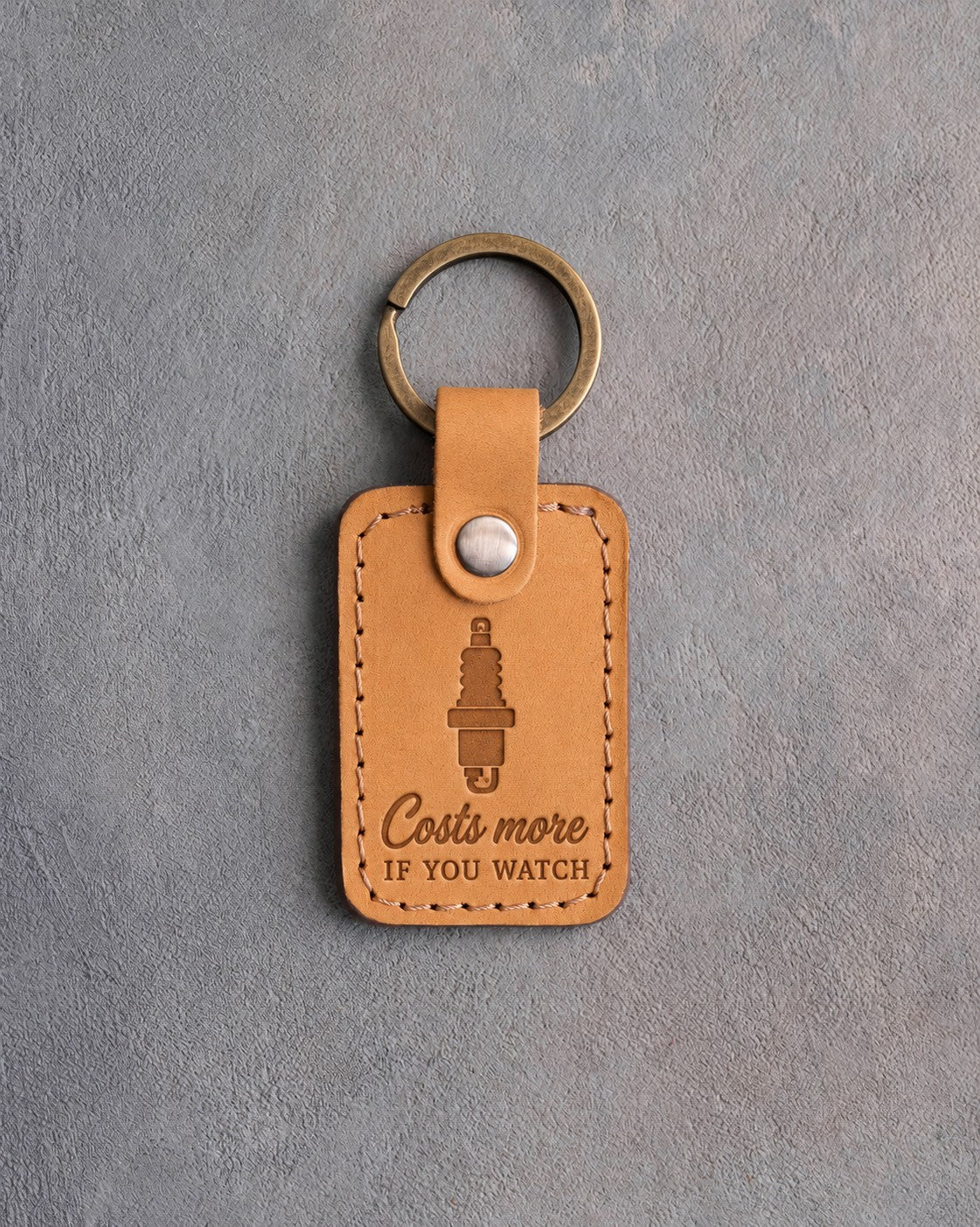 Golden tan leather keychain debossed with a spark plug above Costs more and IF YOU WATCH