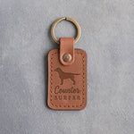 Caramel leather keychain debossed with a Labrador Retriever silhouette and the words Counter SURFER, on gray concrete