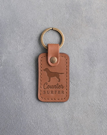 Caramel leather keychain debossed with a Labrador Retriever silhouette and the words Counter SURFER, on gray concrete