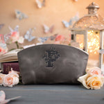 Gray leather makeup bag with a floral monogram, staged among roses on a slate blue table