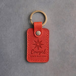 Poppy red leather keychain debossed with a spur rowel above Cowgirl and SINCE DAY ONE, on gray concrete