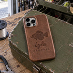 Sicilian brown Lyle CRAPPIE iPhone case in full-grain leather on the lid of an olive-green steel tackle box in a garage, lures in the trays behind