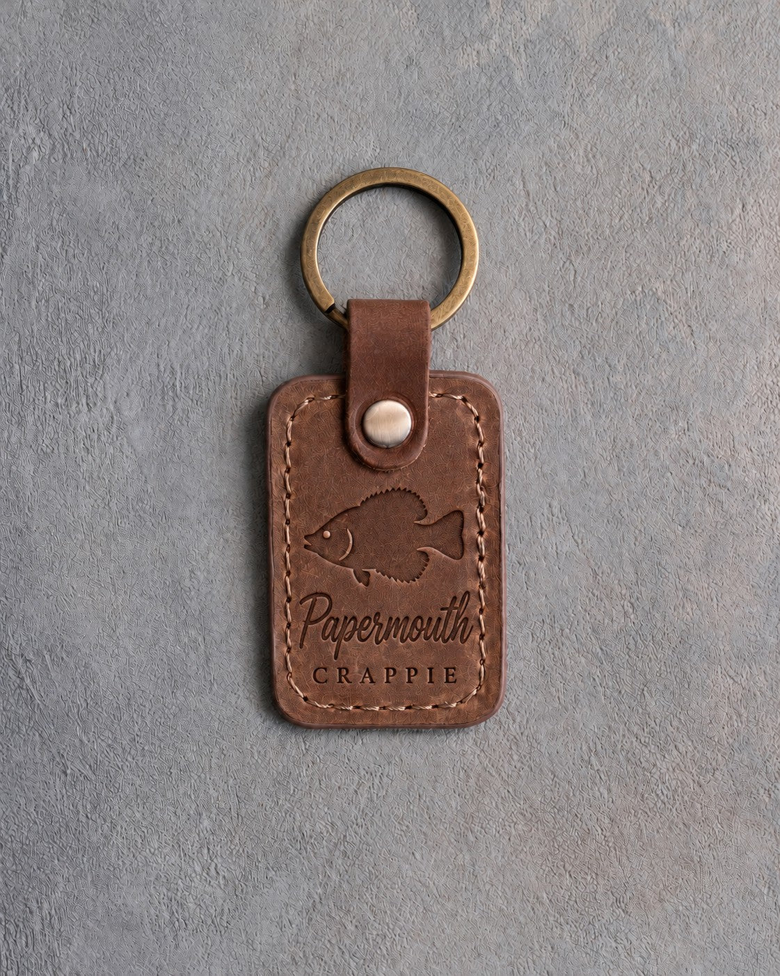 Sicilian brown leather keychain debossed with a crappie above Papermouth and CRAPPIE, on gray concrete