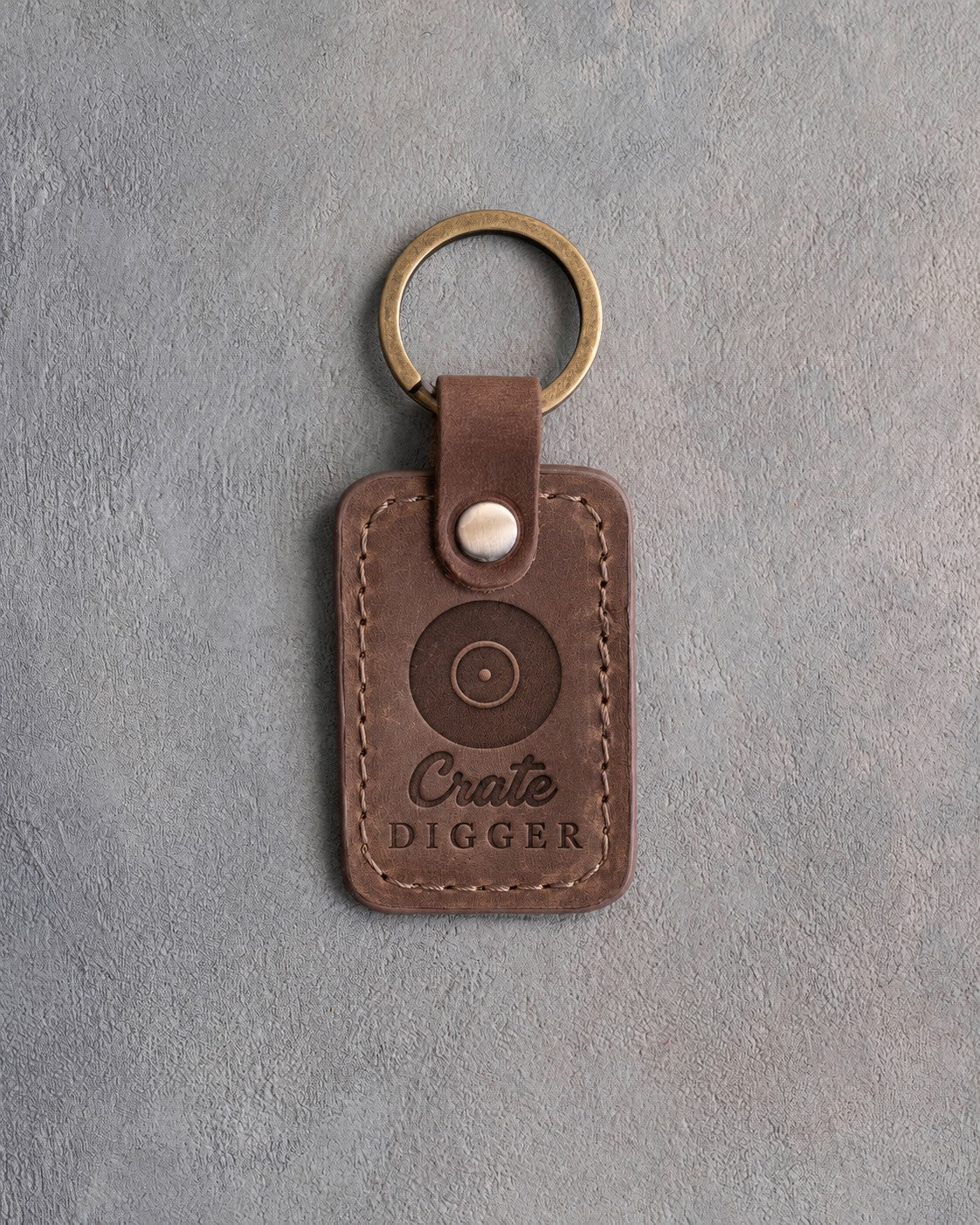 Sicilian brown leather keychain debossed with a vinyl record above the words Crate DIGGER, on gray plaster