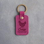 Fuchsia leather keychain debossed with a plump hen above the words Crazy CHICKEN LADY, on gray concrete