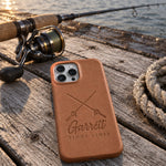 Caramel Garrett TIGHT LINES iPhone case in full-grain leather on sun-bleached dock boards beside a spinning rod in low evening sun