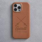 Back of a caramel leather iPhone case debossed with crossed fishing rods above Garrett and TIGHT LINES below the camera, on gray plaster
