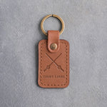 Caramel leather keychain debossed with crossed fishing rods above TIGHT LINES, on gray concrete