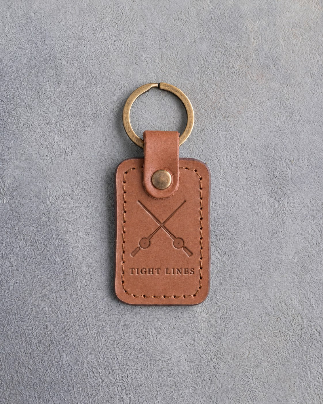 Caramel leather keychain debossed with crossed fishing rods above TIGHT LINES, on gray concrete