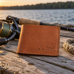 Caramel Garrett TIGHT LINES bifold wallet in full-grain leather on sun-bleached dock boards beside a spinning rod in low evening sun