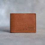 Closed caramel leather bifold wallet with crossed fishing rods beside Garrett and TIGHT LINES pressed in the lower right corner, on gray plaster