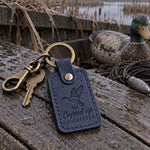 Navy Cupped Up Committed keychain on truck keys resting on a pile of duck decoys in gray morning light
