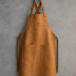 Indian Summer leather bib apron with cross-back straps, chest debossed with a sample business logo, on grey plaster