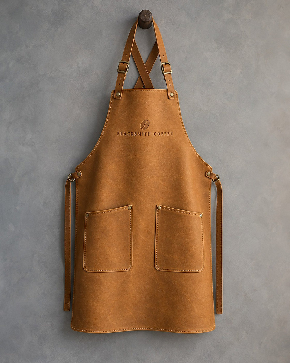 Indian Summer leather bib apron with cross-back straps, chest debossed with a sample business logo, on grey plaster