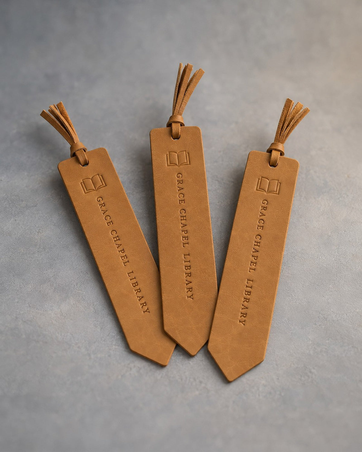 Indian Summer leather bookmarks with tassels debossed with a sample business logo, on a grey plaster backdrop