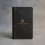 Black leather car document holder with a sample business logo in gold foil, on a grey plaster backdrop