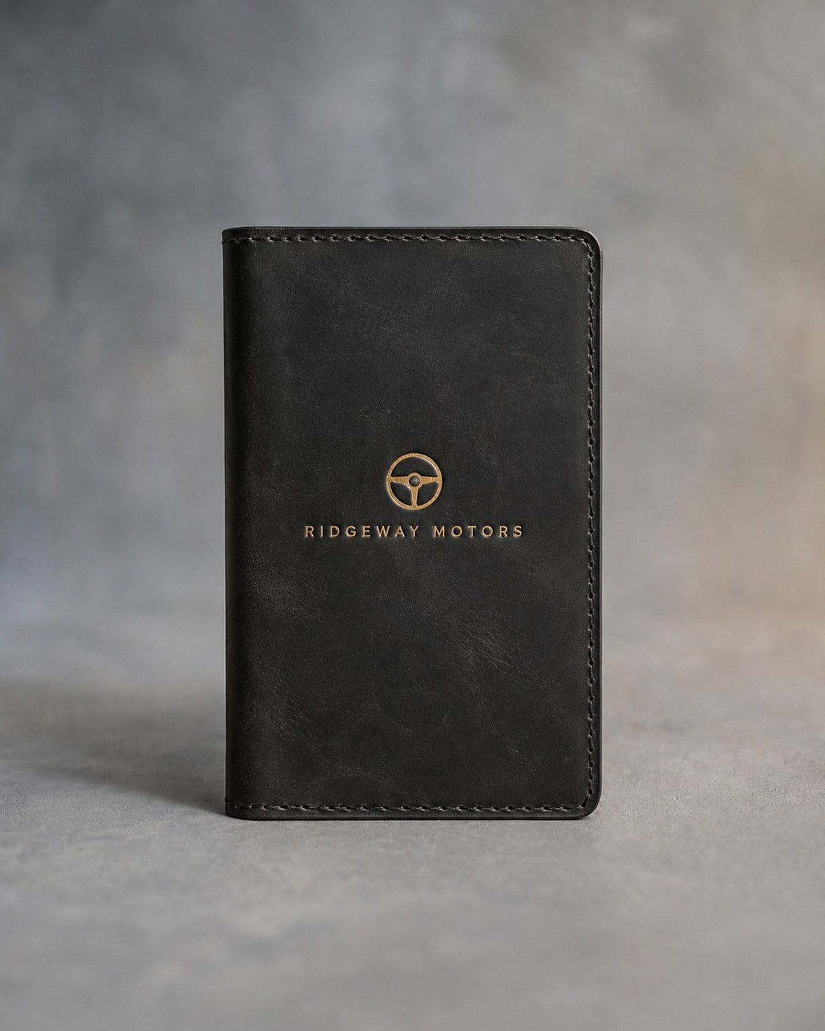 Black leather car document holder with a sample business logo in gold foil, on a grey plaster backdrop